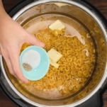 adding salt and pepper to uncooked elbow pasta, chicken stock, and butter in the instant pot