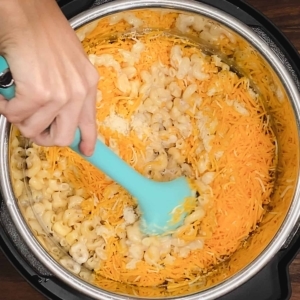 mixing cooked elbow pasta, cream of mushroom soup, parmesan, and shredded cheddar cheese with a large silicone spoon in the instant pot