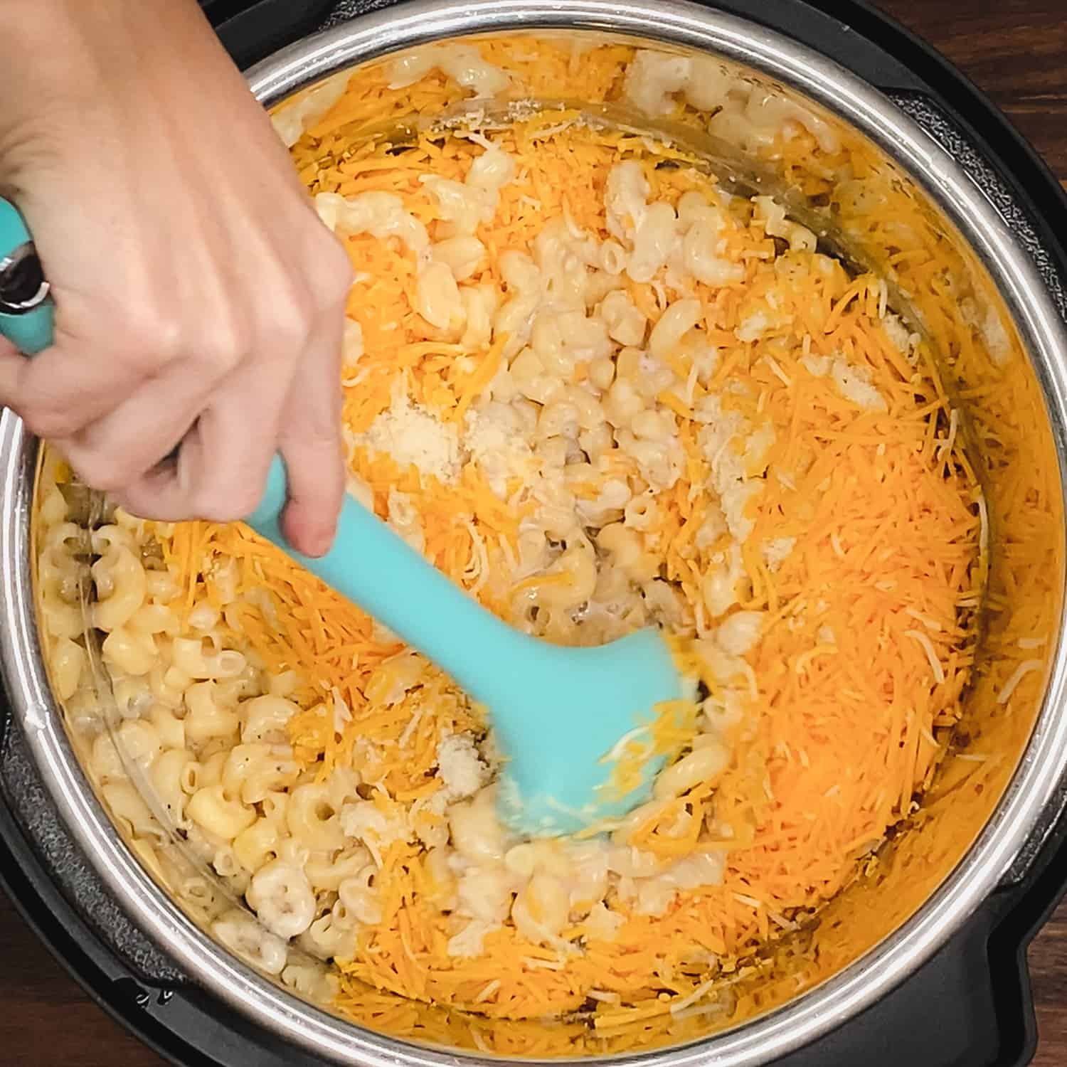 mixing cooked elbow pasta, cream of mushroom soup, parmesan, and shredded cheddar cheese with a large silicone spoon in the instant pot