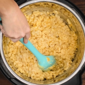 mixing cooked elbow pasta, cream of mushroom soup, parmesan, and shredded cheddar cheese with a large silicone spoon in the instant pot