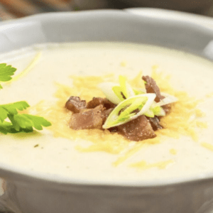 a bowl of cauliflower chowder topped with cheese, bacon, and chives