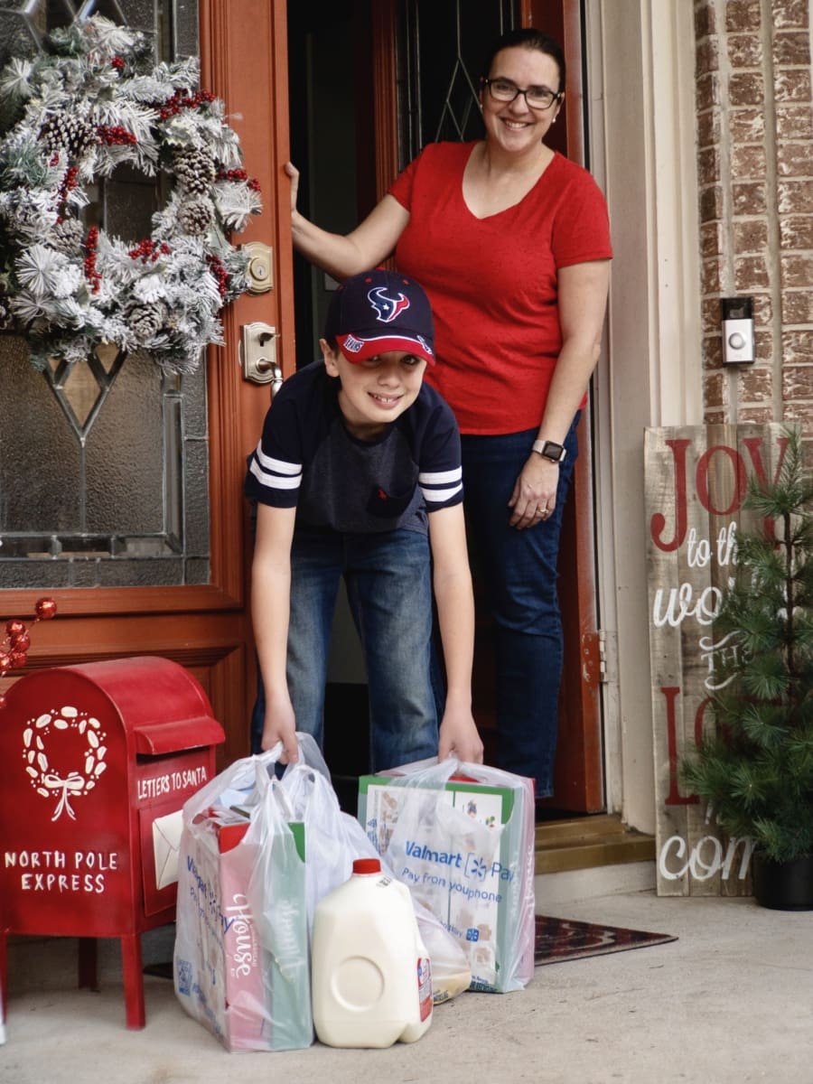 a young boy picking up bags of groceries delivered by Walmart to the front porch