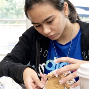 a young girl building a gingerbread house using icing