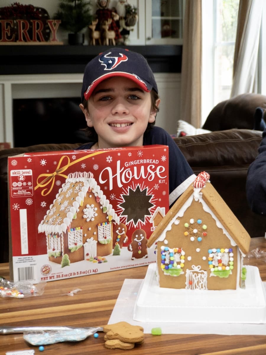 a young boy posing with the gingerbread house that he built