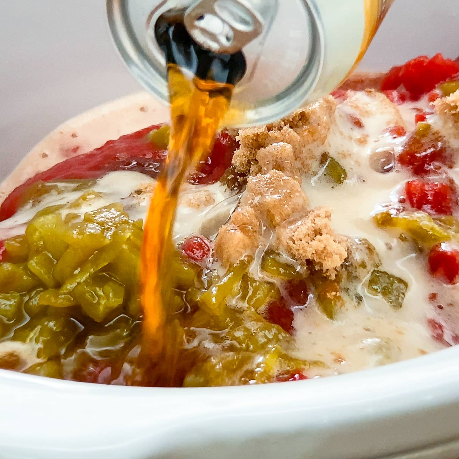 pouring a can of beer over the ingredients for carne mechada in the crockpot