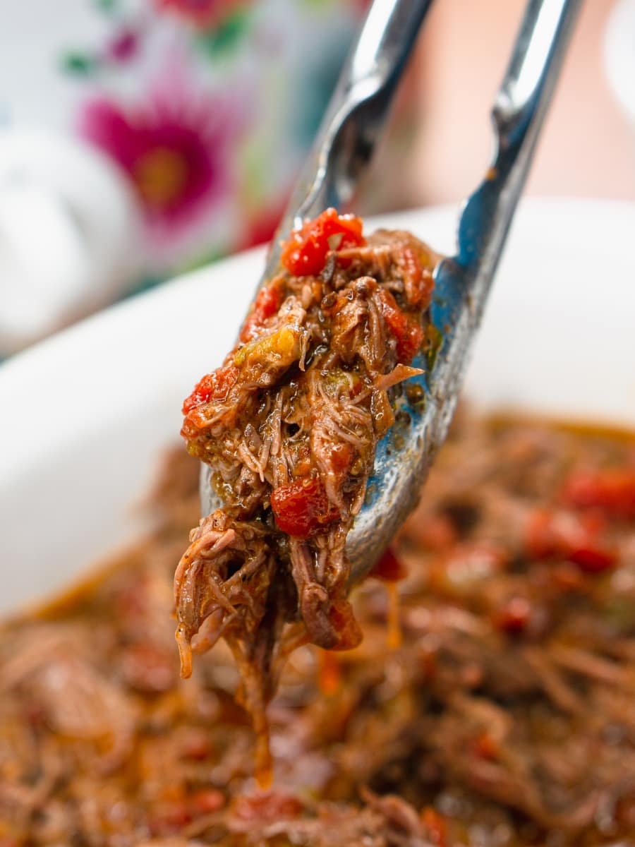 grabbing carne mechada from the slow cooker with tongs