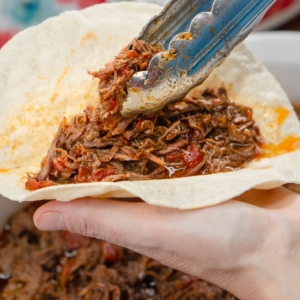 placing carne mechada on a flour tortilla to make a taco