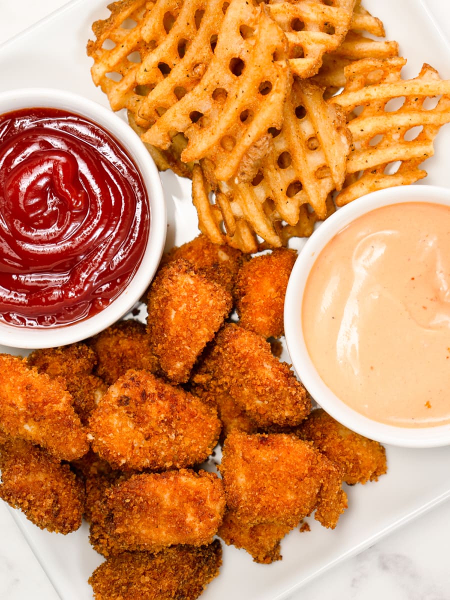 a plate of chicken nuggets and waffle fries with ketchup and dipping sauce