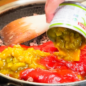 adding diced green chiles to ground beef and sloppy joe sauce in a skillet