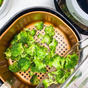 adding seasoned broccoli to the air fryer basket for roasting