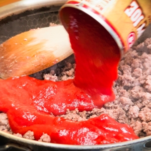 adding sloppy joe sauce to a skillet of cooked ground beef