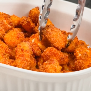 placing breaded chicken nuggets in a serving dish with tongs