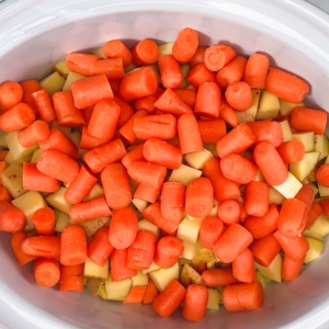 pot roast ingredients including cubed sweet potatoes, yellow potatoes, and carrots in the slow cooker