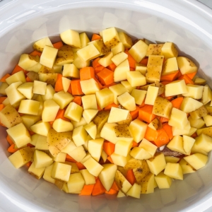 pot roast ingredients including cubed yukon gold yellow potatoes with sweet potatoes and a seasoned chuck roast in the slow cooker