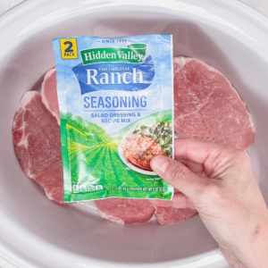 holding a packet of ranch seasoning over a slow cooker filled with pork chops before making ranch pork chops