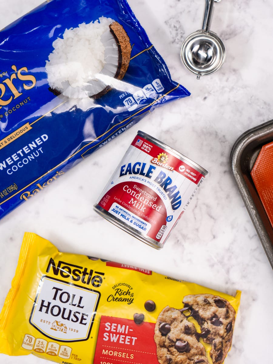 ingredients for chocolate chip coconut macaroons including a can of sweetened condensed milk, a bag of sweetened coconut, and a bag of semi-sweet chocolate morsels