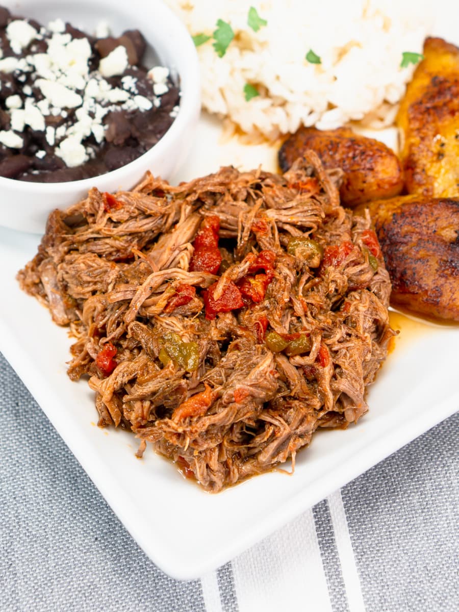 carne mechada served on a plate with black beans, fried plantains, and white rice