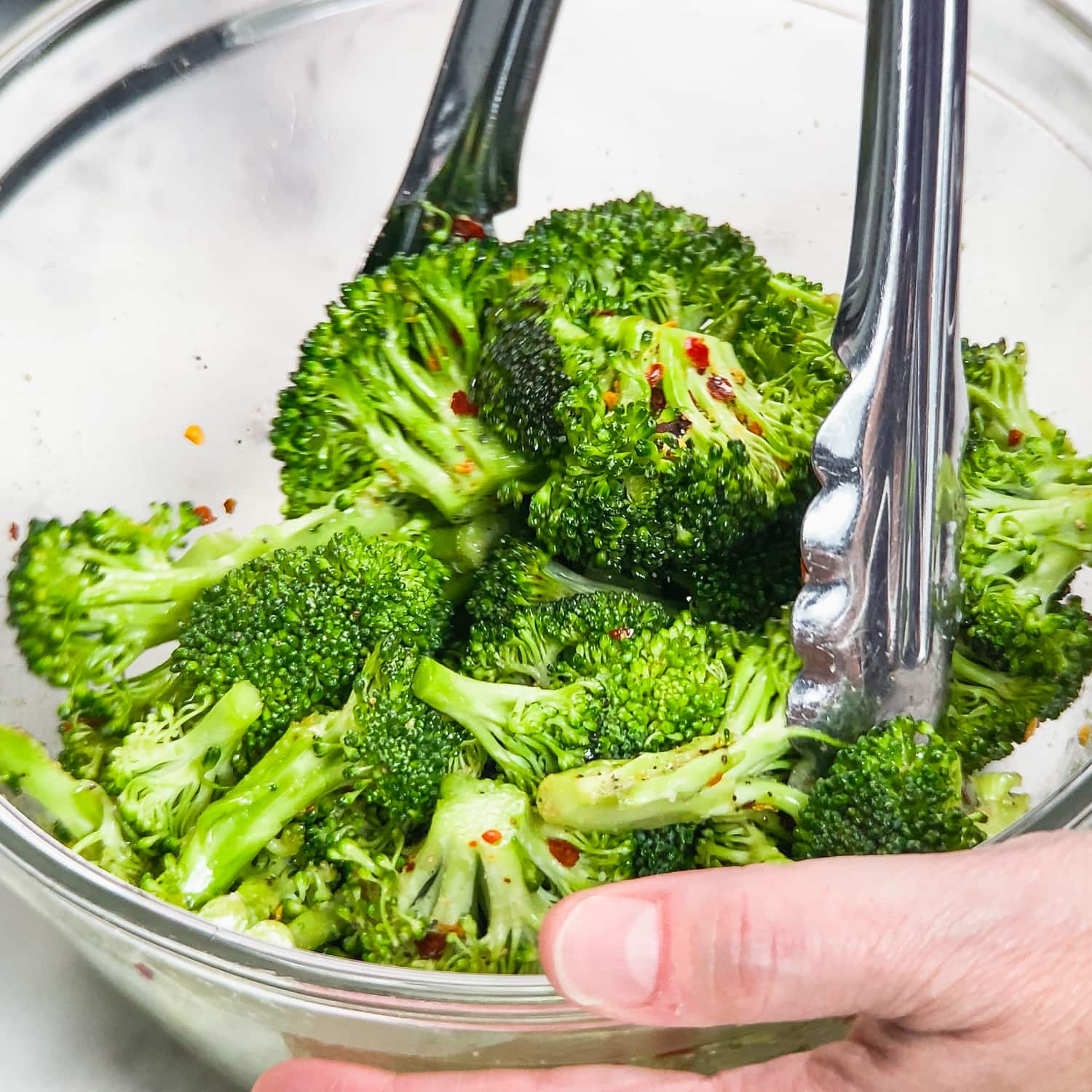 mixing broccolii with seasoning in a glass bowl