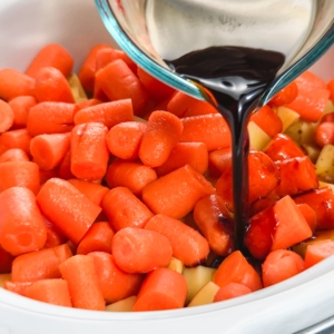 pouring soy sauce over ingredients (carrots, potatoes, roast) in the slow cooker for making a pot roast