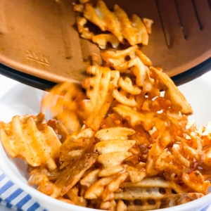 pouring waffle fries from air fryer basket to bowl