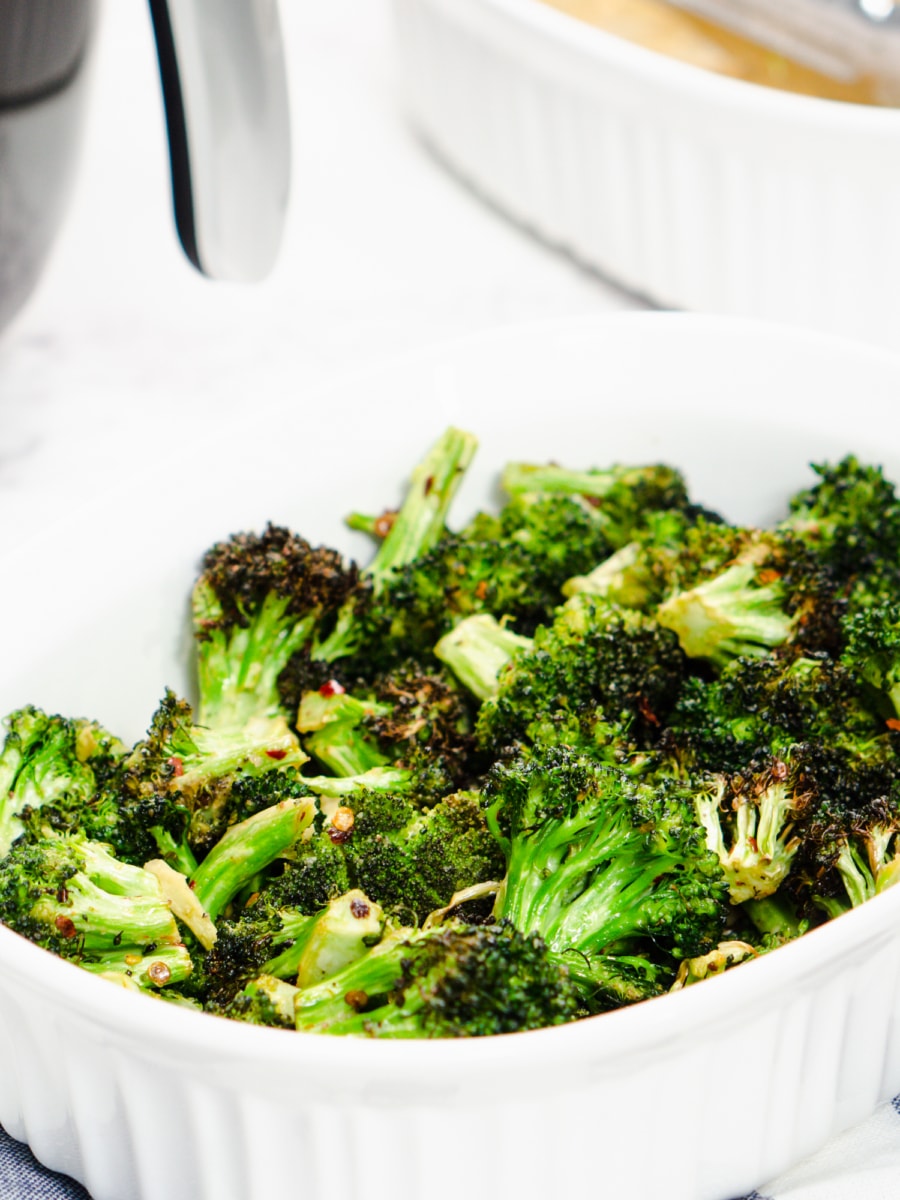 roasted broccoli in a serving dish with an air fyer in the background