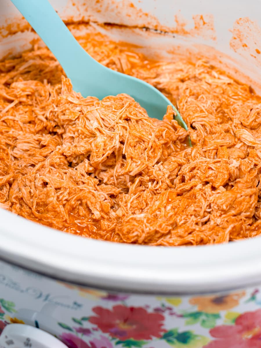 scooping up a large spoonful of shredded buffalo chicken from the slow cooker