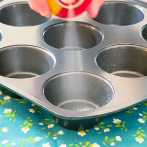 spraying a cupcake pan with oil