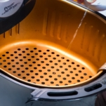 spraying air fryer basket with avocado oil before making sweet potato fries