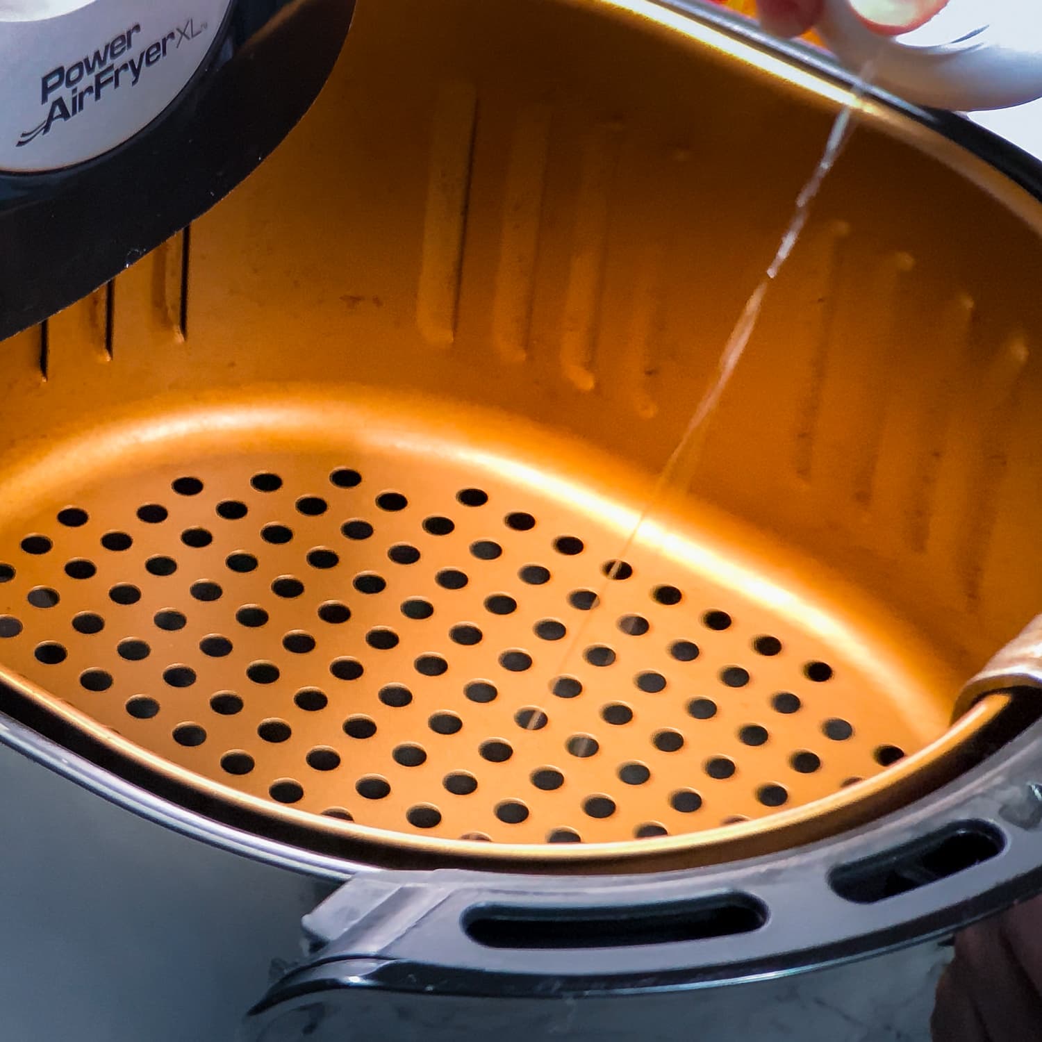 spraying air fryer basket with avocado oil before making sweet potato fries