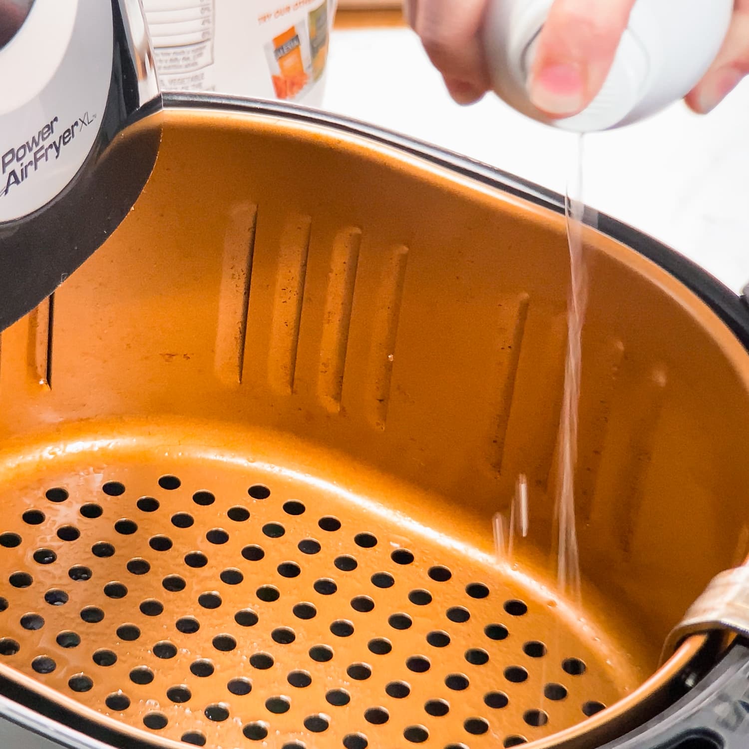 spraying air fryer basket with avocado oil