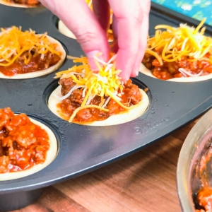 topping sloppy joe cornbread cups with shredded cheddar cheese