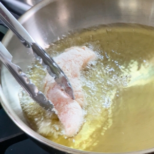 adding a chicken tender to hot oil in a skillet