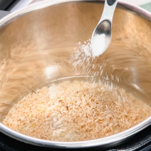 adding salt to brown rice and water in the pressure cooker