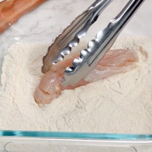 dredging a chicken tender in gluten-free breading