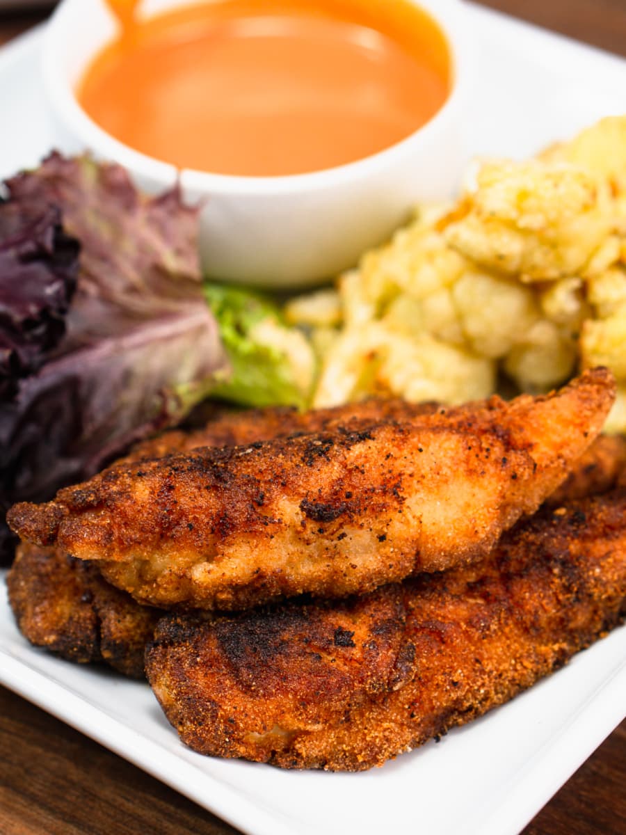 gluten free chicken tenders on a plate with cauliflower, gluten free dipping sauce, and a salad