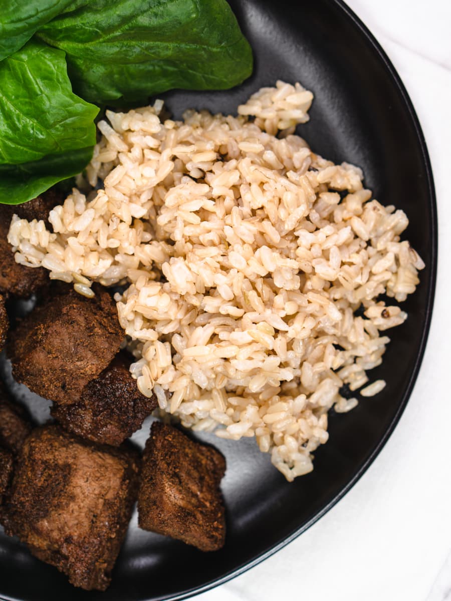 instant pot brown rice served on a plate with beef and a salad