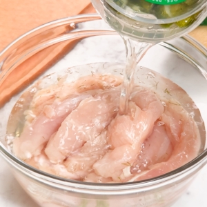 pouring pickle juice over chicken tenders in a mixing bowl to marinate them