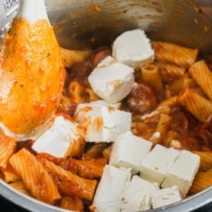 adding cubes of cream cheese to the instant pot and mixing it into the hot pasta until it melts