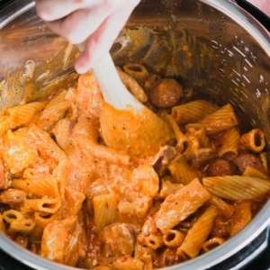 mixing cooked pasta, sausage, and other ingredients for cream cheese pasta in the instant pot