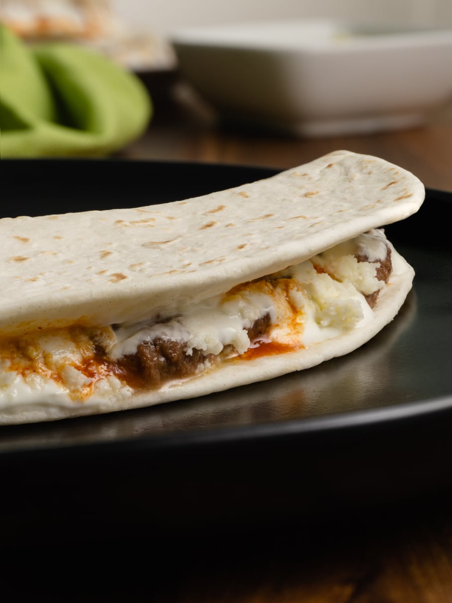 side view of a closed honduran baleada filled with beans, mantequilla, hot sauce, and cheese