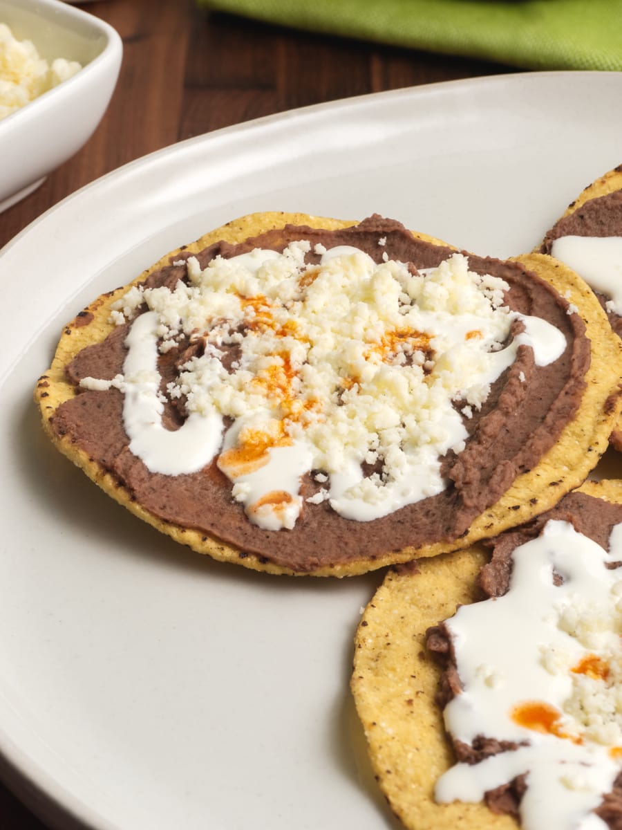 a plate of tostadas or toasted tortillas with refried beans, mantequilla, cheese, and hot sauce