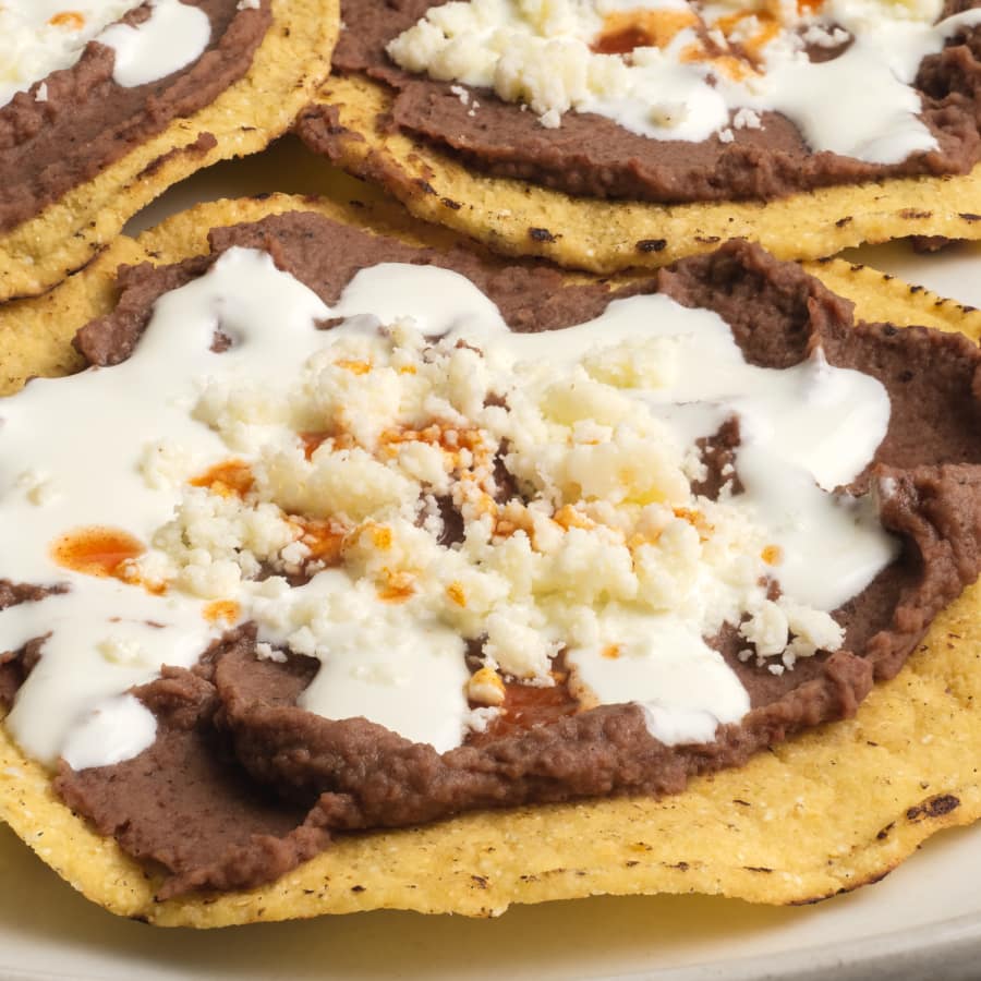 close up of bean and cheese tostada drizzled with mantequilla and hot sauce