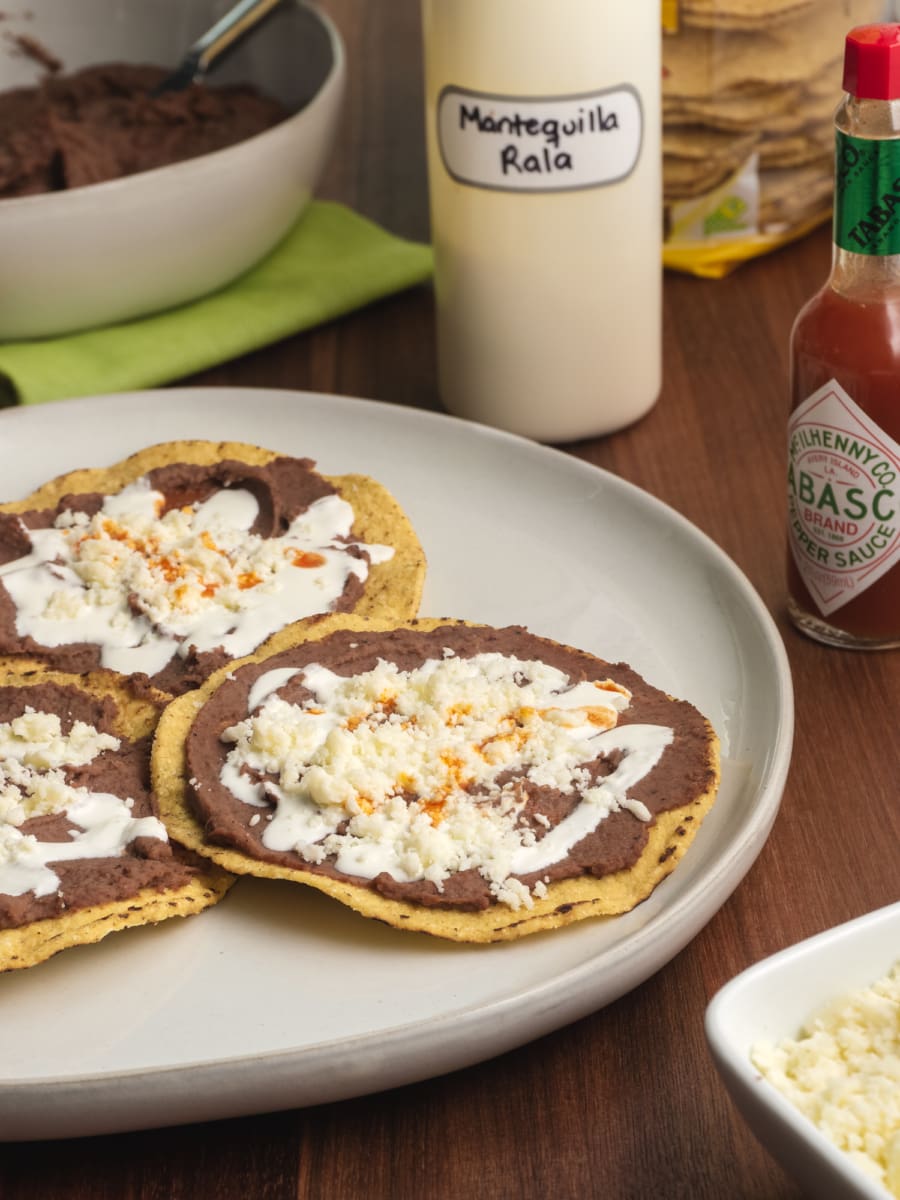 a plate of homemade tostadas with refried beans topped with mantequilla, cheese, and hot sauce