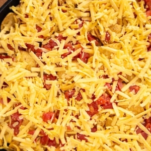 layers of corn chips, canned chili, rotel, and cheddar cheese in a large skillet ready to bake