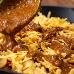 adding a second layer of canned chili over fritos and shredded cheese in a large skillet