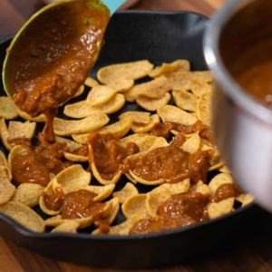 spooning warm chili over fritos corn chips