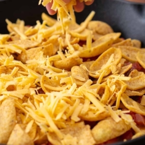 shredded cheddar cheese being evenly layered over fritos corn chips